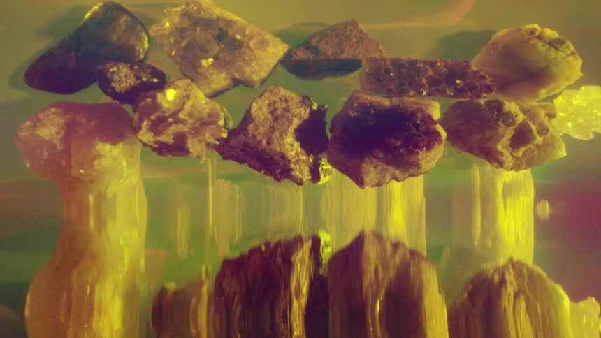 Abstract and illuminated various sizes of dark roughedged rocks are submerged on a reflective rippled surface glowing with yellow and orange light