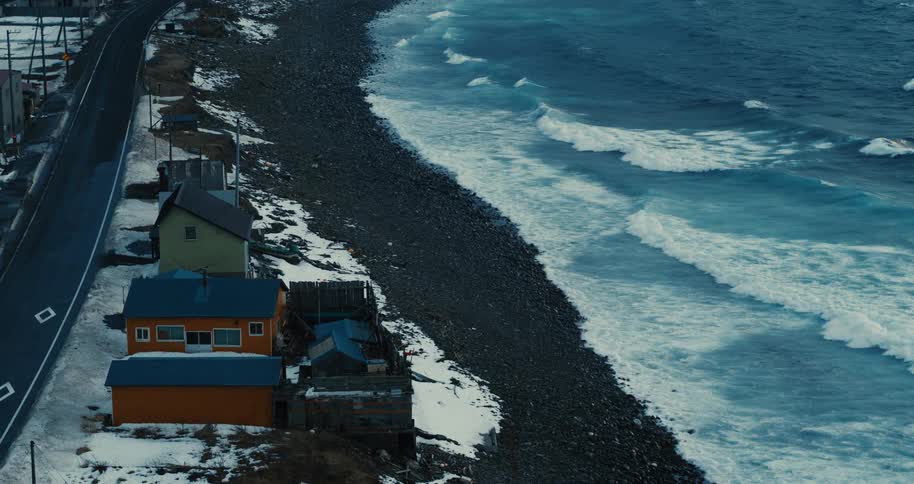 Coastal homes line a snowy shore as waves crash under gray skies