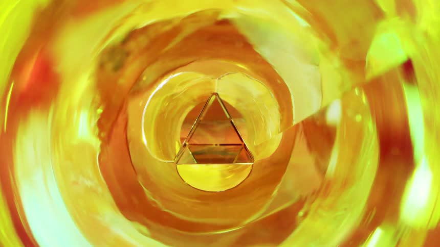 A mesmerizing abstract view features a crystal pyramid at the center of a swirling golden yellow glass vortex