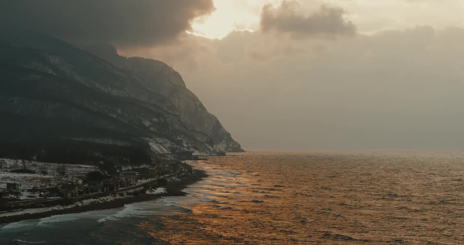 Golden sunset reflects off ocean by a moody mountain coast