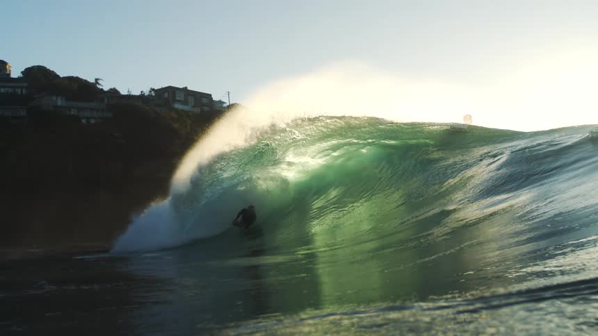 A couple people surf a large wave