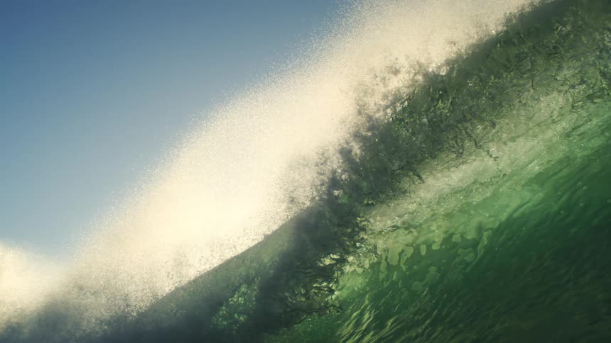 A cresting wave curls into a glowing water tunnel before crashing down and fully submerging the view beneath a rush of foam and turbulence