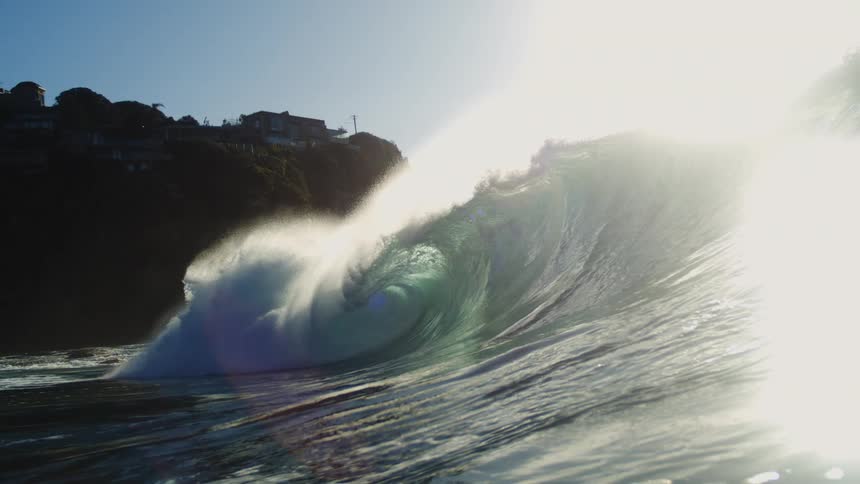A large wave crashes near a cliff