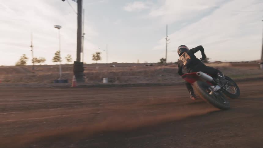 A motocross rider rides on a sandy race track at sunset