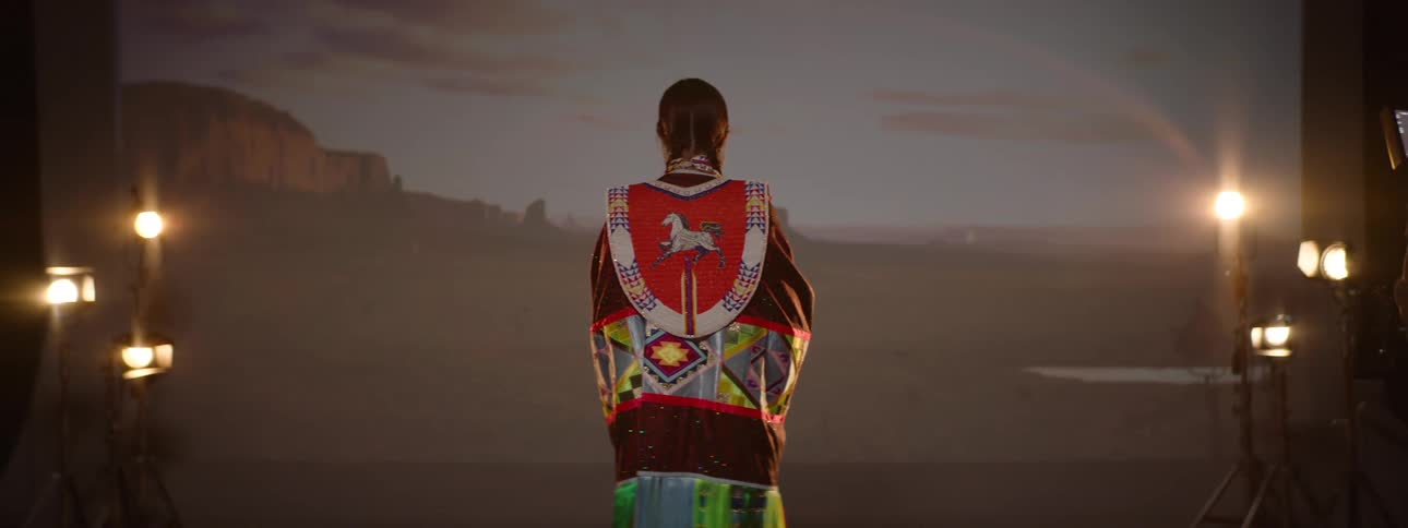 Woman wears a colorful native american outfit while posing in front of a photography backdrop