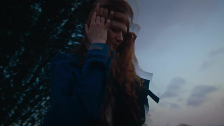 Redheaded woman running her hand through her hair while walking in a natural setting