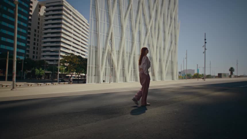 A woman stands alone on an empty city street near a modern glass building