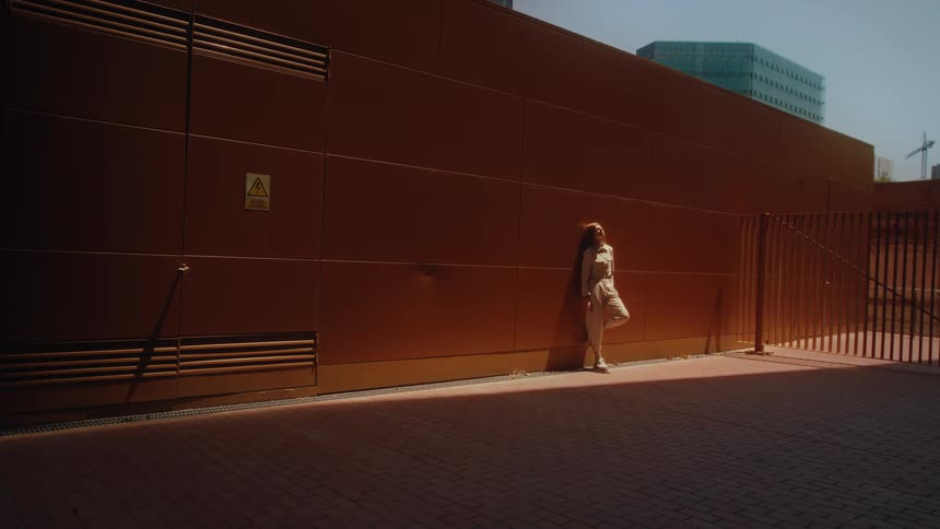 Woman leaning against the exterior wall of a building walks away from the building on a sunny day