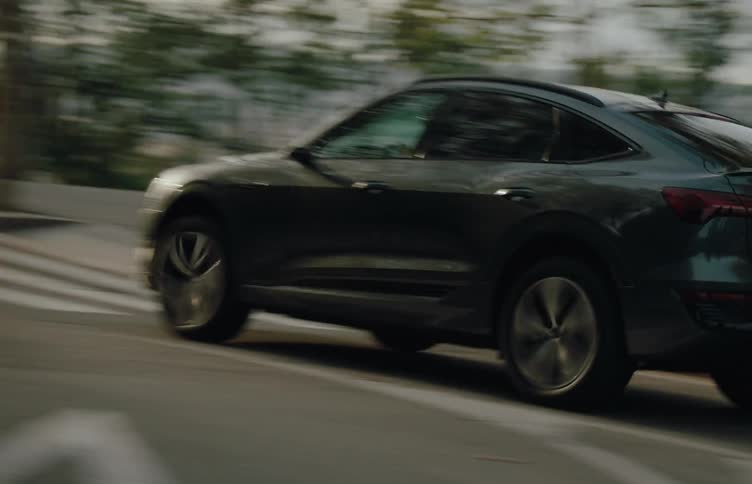 A grey car speeds past on a crosswalk with blurred treelined hills in the background