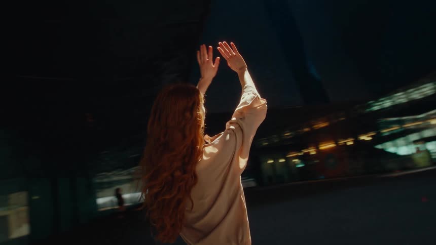 A woman raises her arms above her head by the building