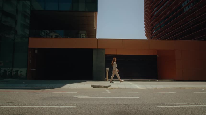 A woman walks down a sidewalk past two large buildings