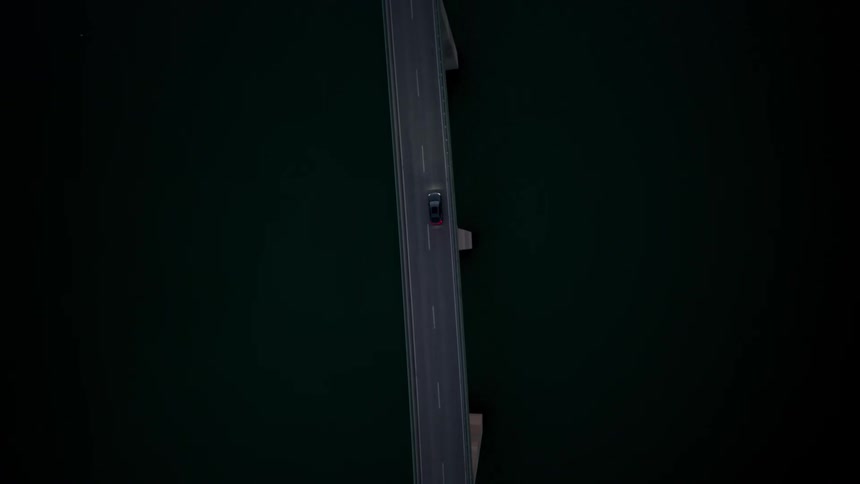 A single car drives on a bridge going over a large calm river at night