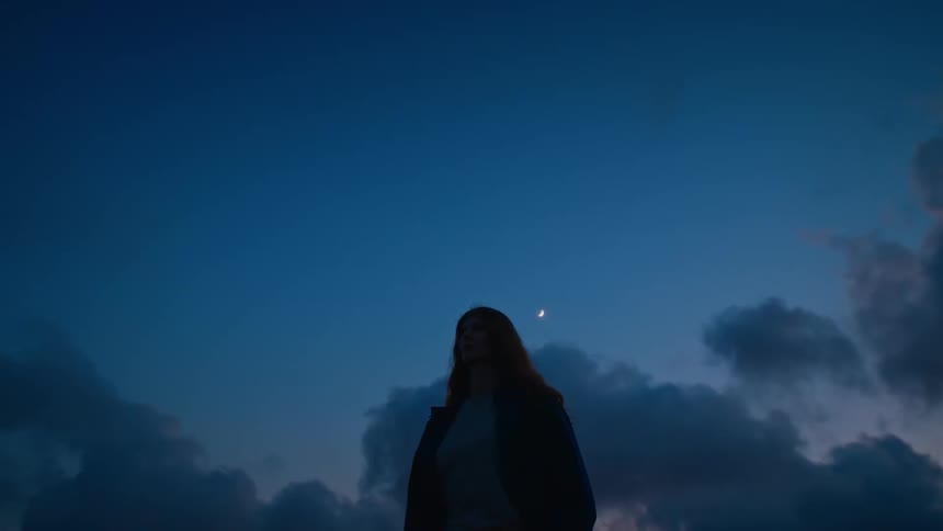 Time lapse of a woman standing still with the sky and clouds behind her