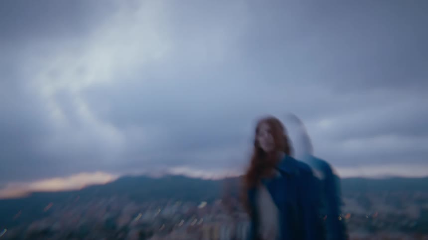 A woman is slowly dancing on top of a hill in front of a suburban neighborhood