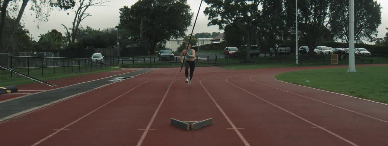 A lady practicing pole vaulting on a race track in the morning