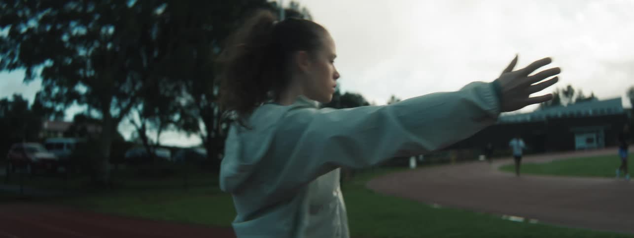 A woman stretches her arms forward while warming up on an outdoor track field