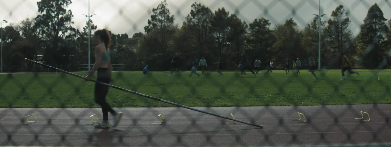 A young woman is running down a sports track carrying a huge stick and then she stops and starts walking back where she came from
