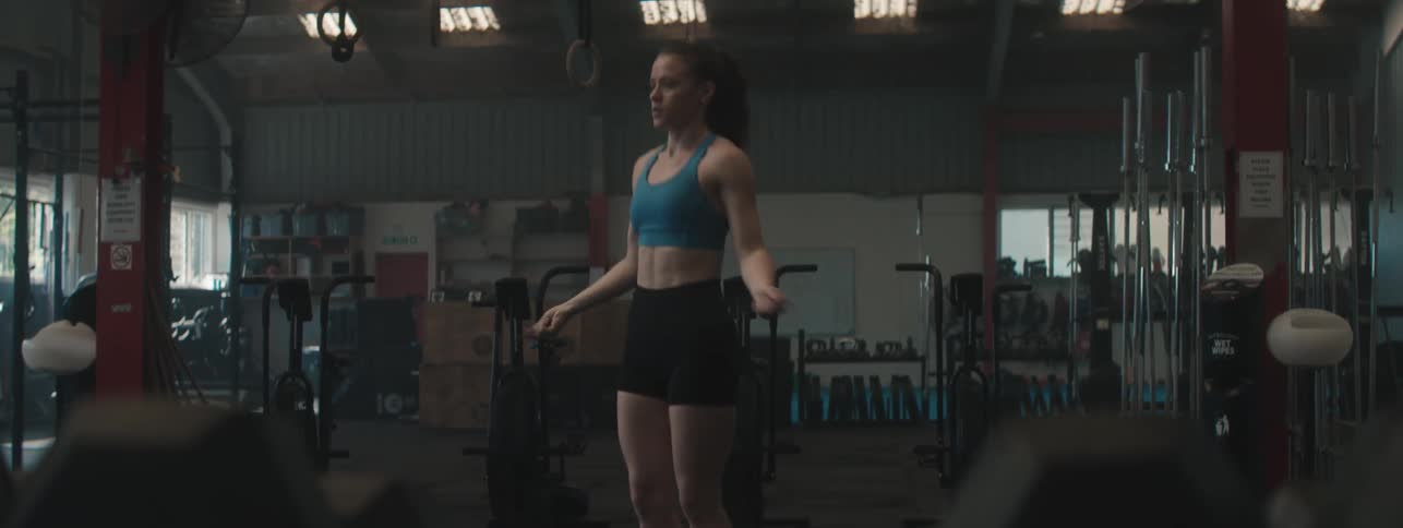Woman in athletic wear skips rope alone in a dimly lit gym