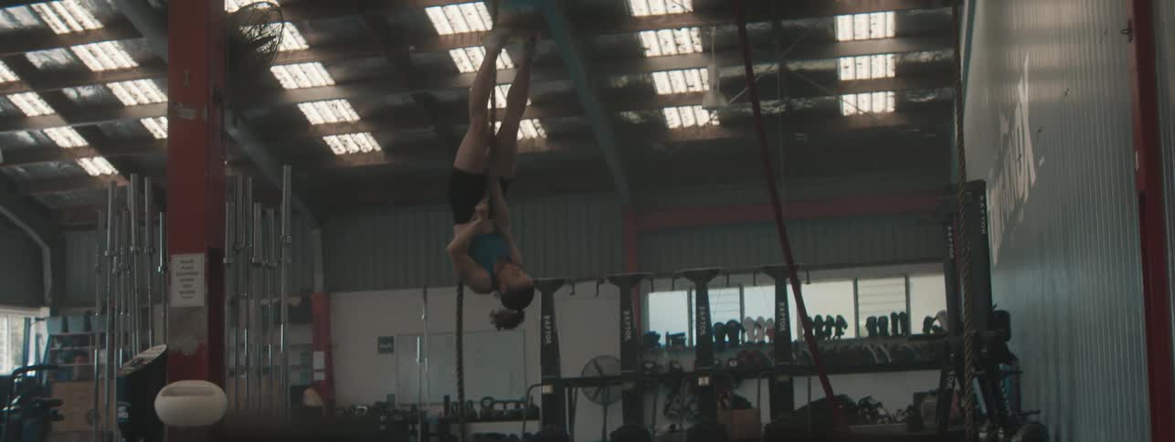 A woman hangs upside down from gym ropes midair in a fitness training facility