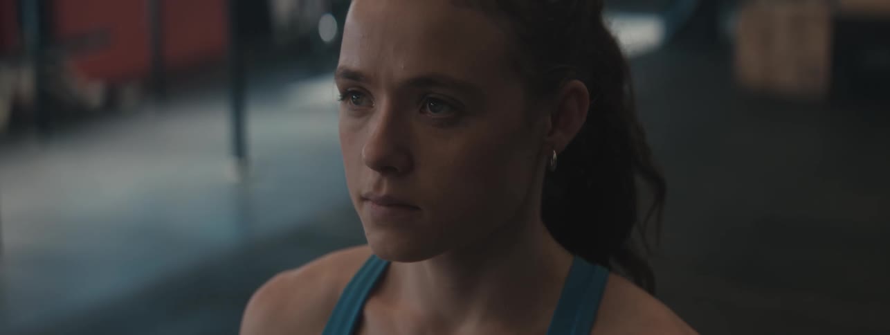 A young woman at the gym does pullups hanging from a bar at midday