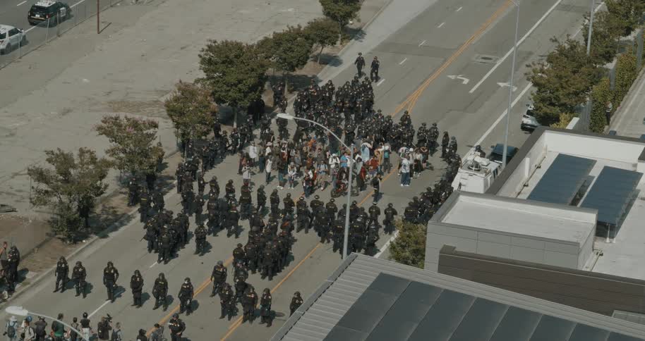 Police officers stand around crowds of people on an urban street during the daytime