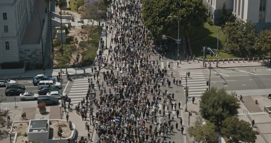 A large crowd of people is actively protesting in the streets in los angeles holding numerous signs and banners