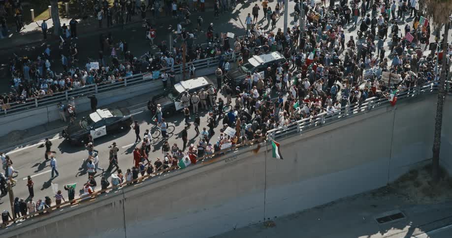 A large crowd of people is actively protesting in the streets of los angeles holding numerous signs and banners