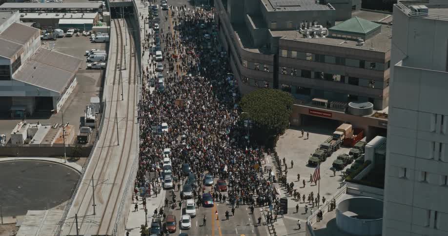 A peaceful protest fills a city street outside a hospital watched by military vehicles and troops