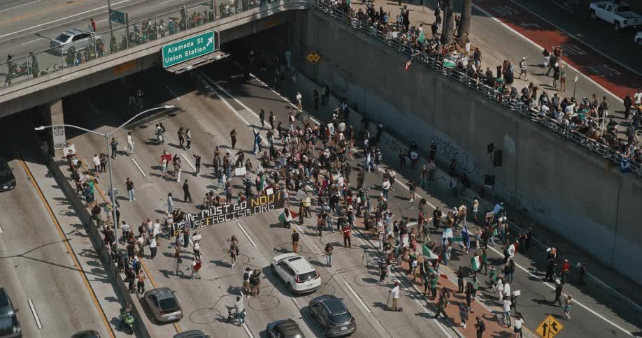 Large crowd protesting on a city freeway beneath an overpass holding banners and signs