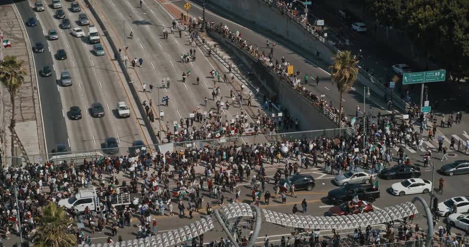 An aerial view shows a massive crowd of protesters marching blocking city streets and spilling onto a major freeway