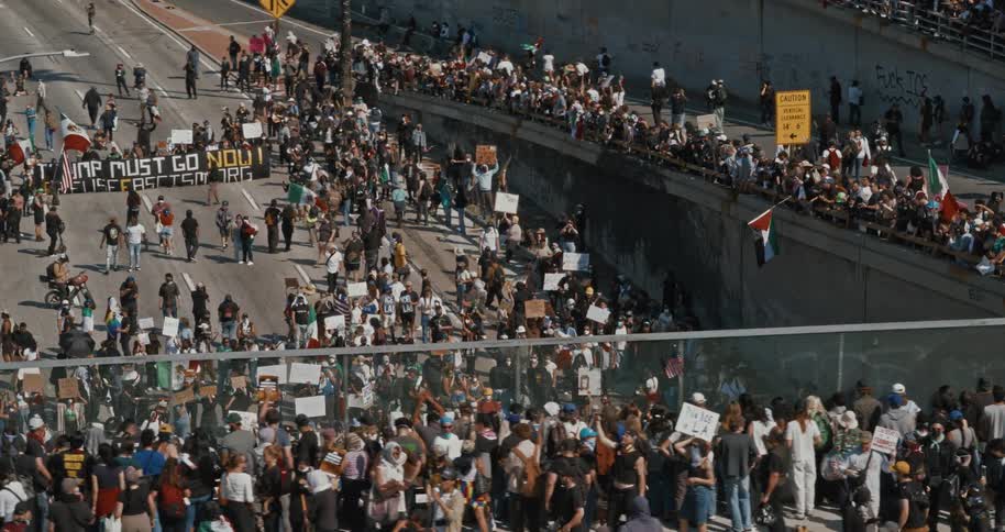 A large group of people are protesting on a highway holding signs and banners with one prominent banner
