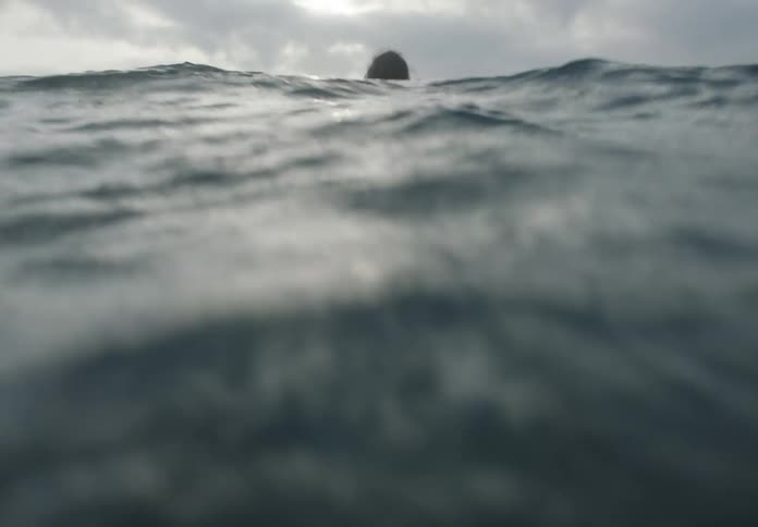 A person swims in the ocean wearing a life jacket at midday