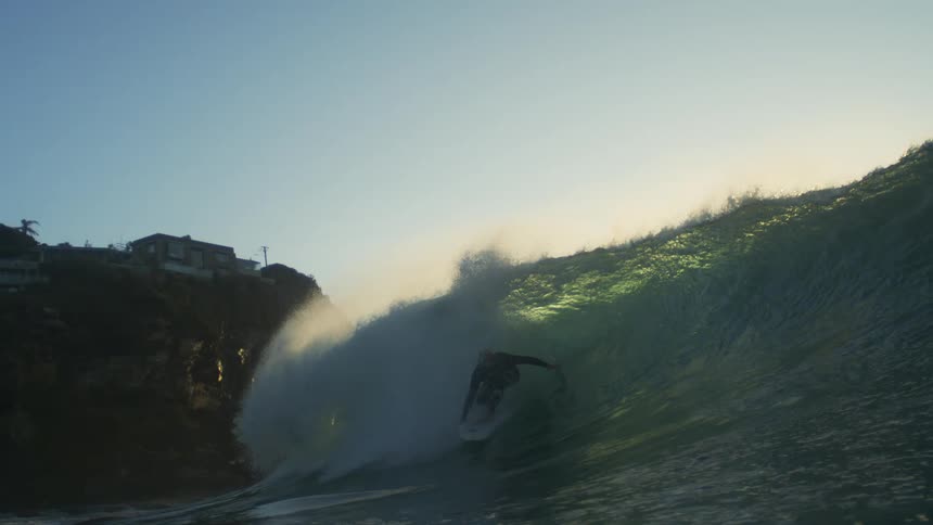 A surfer is riding a huge wave towards the island shore