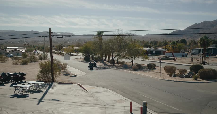 Motorcyclists ride through a quiet desert neighborhood under a clear sky