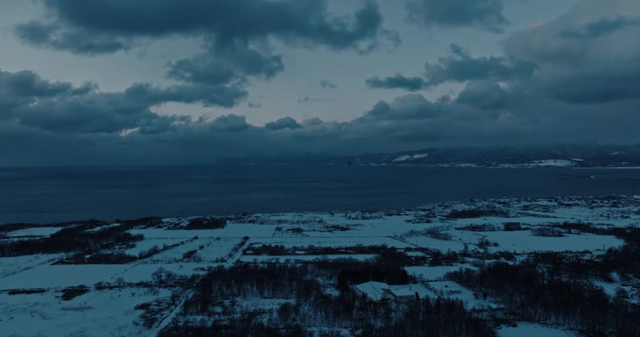 Storm clouds loom over a desolate area with snow covered grass