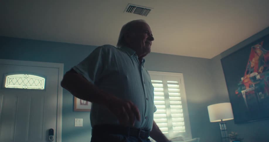 An elderly man smiles and dances while standing in a living room