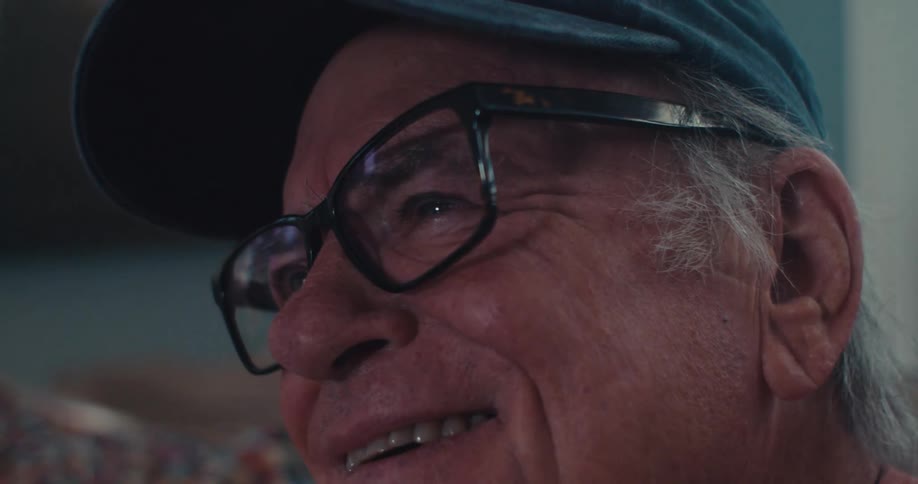 Close up of an elderly mans face as he smiles while watching tv in a living room