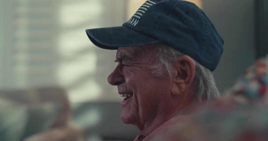Close up of an elderly man laughing continuously while watching tv in a living room