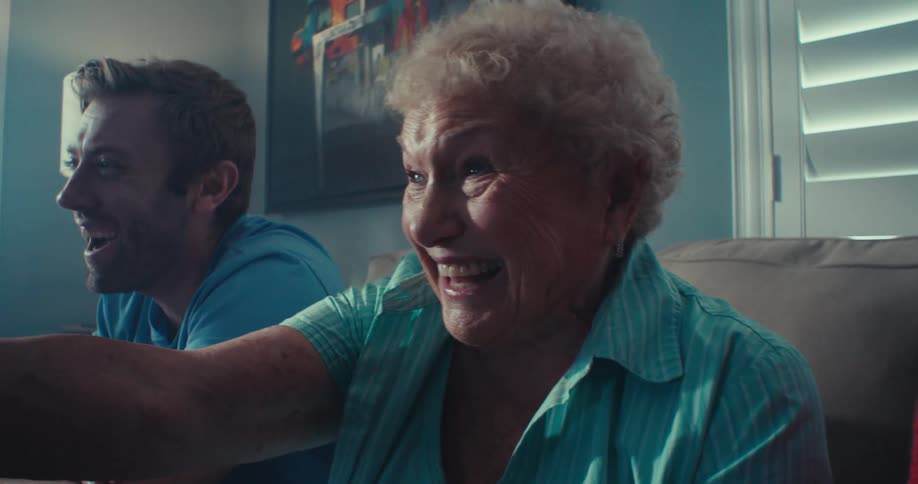 An elderly woman and a young couple sit on a couch in a living room enjoying a television show together