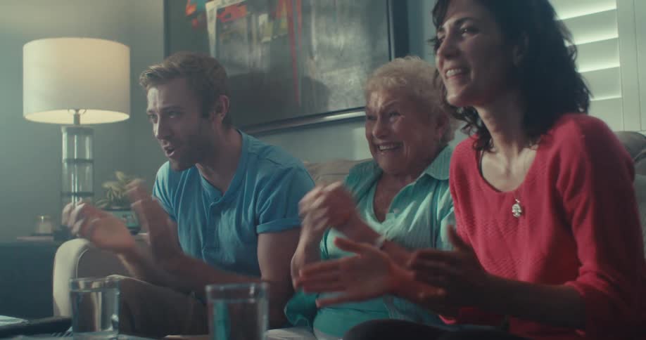 An elderly woman sits between a young couple on a couch at midday as they all laugh and enjoy a good time together