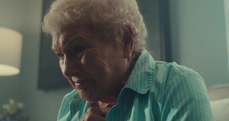 Close up of an elderly woman anxiously watching media on a device while sitting in a living room