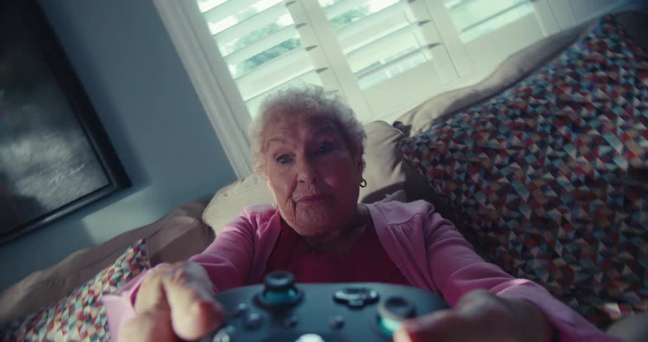 An elderly woman intensely plays a video game with a focused expression