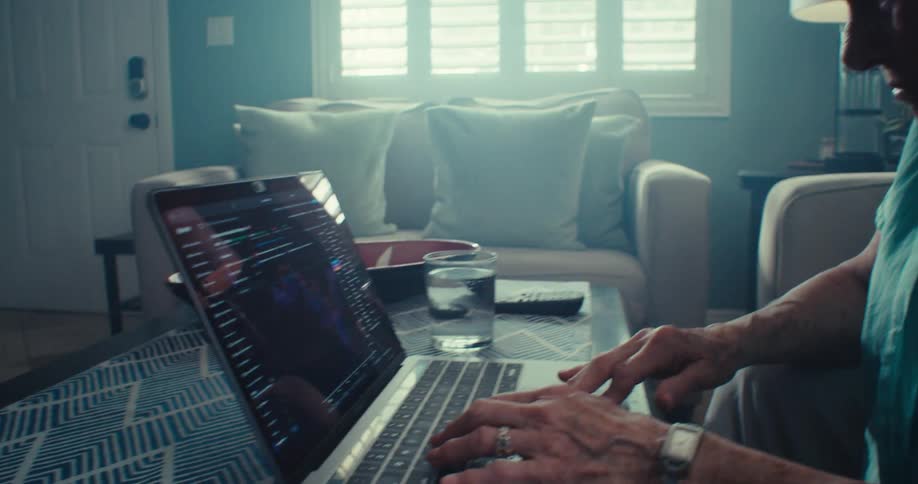 Elderly woman operates a laptop computer on a table in a living room