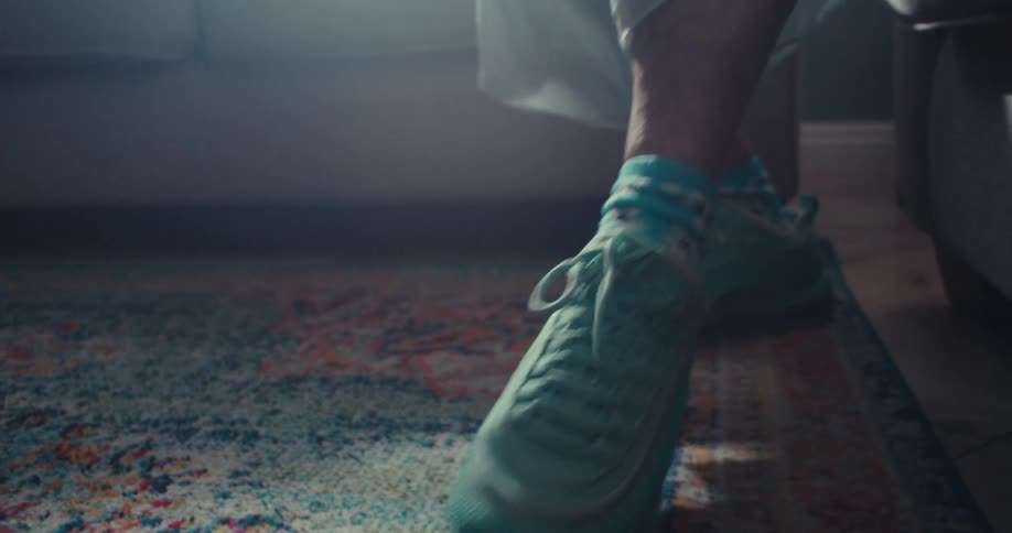 A person wearing blue sneakers dances on a rug indoors