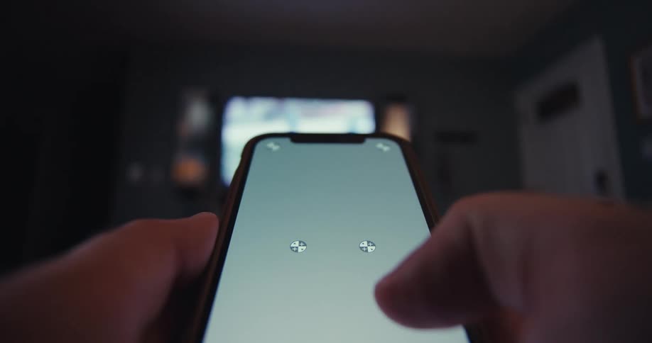 A person holds a smartphone indoors swiping through it with a tv display in front