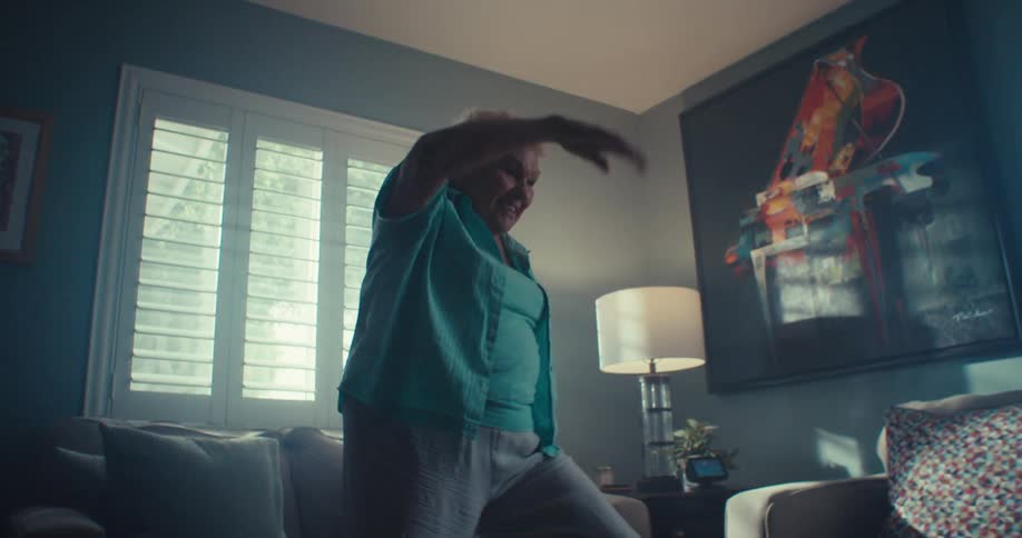 An elderly woman dances happily in a cozy sunlit living room