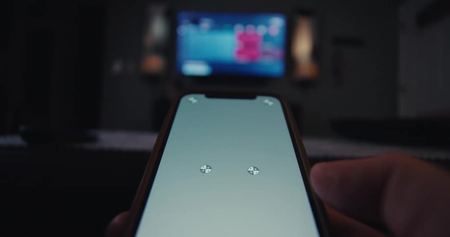 A person uses a smartphone to control a tv screen in a dark room