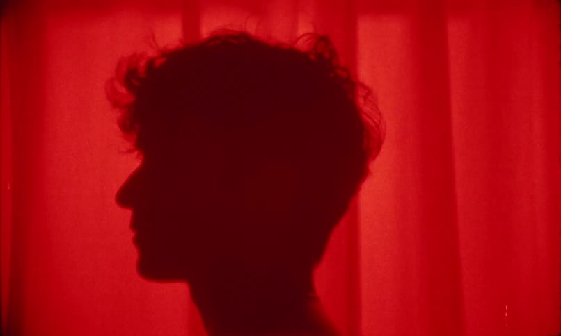 Silhouette of a young man stands against a glowing red curtain backdrop