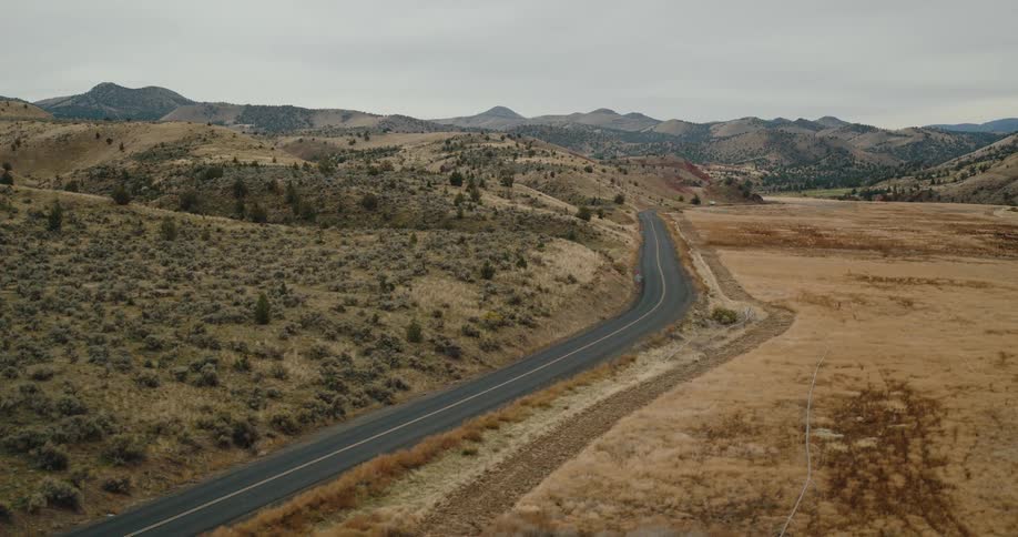 A winding road cuts through a dry hilly landscape under an overcast sky