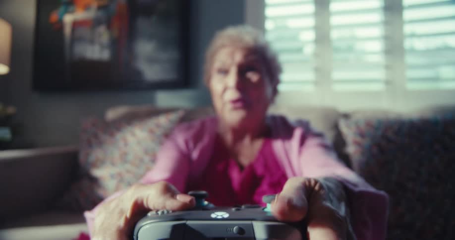 An elderly woman smiles and laughs as she plays video games